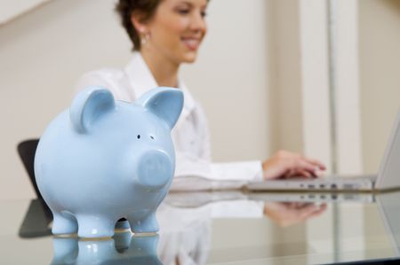 Piggy bank in front of a woman working on a computer.