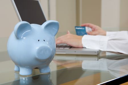 Piggy bank in front with woman ordering on line with credit card.