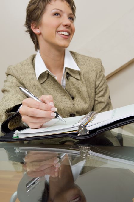 Close-up of a businesswoman at a glass desk with a planner.