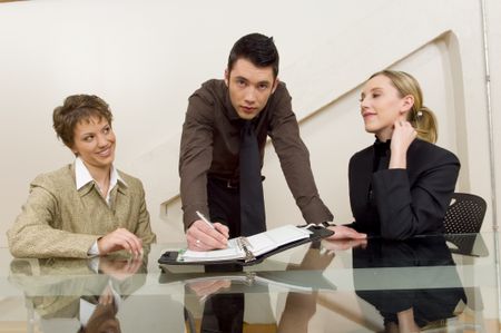 Guy writing in planner with associates looking on.