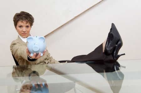 Attractive businesswoman holding piggy bank out over glass desk