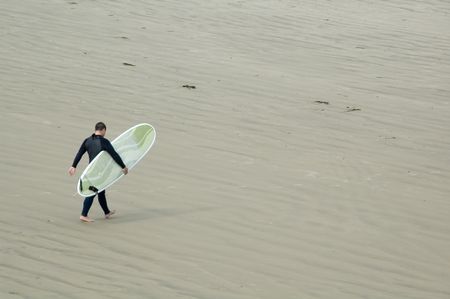 Adult male surfer carries stylish surfboard across sandy beach toward shallow waves