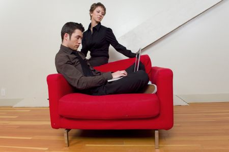 Couple hanging out on red chair  looking at a laptop.