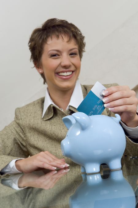 Businesswoman smiling and putting a credit card in piggy bank.