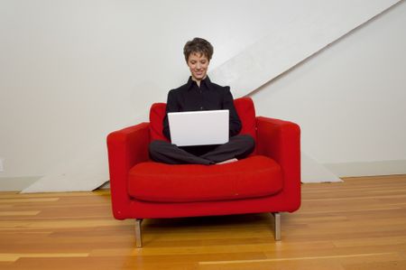 Businesswoman sitting in a red chair working on laptop.