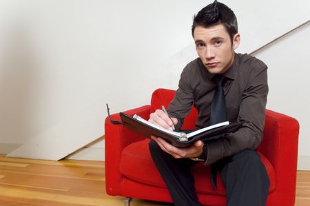 Guy on red chair writing in day timer.