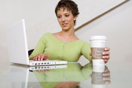 woman working on a computer with a coffee. (focus on coffee)