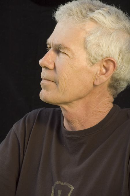 Distinguished mature white man in dark T-shirt, gray hair, dark background, side view