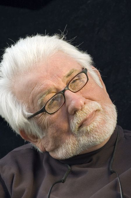 Distinguished mature man with white beard and mustache, eyeglasses, head tilted, looking thoughtfully upward, like a film director