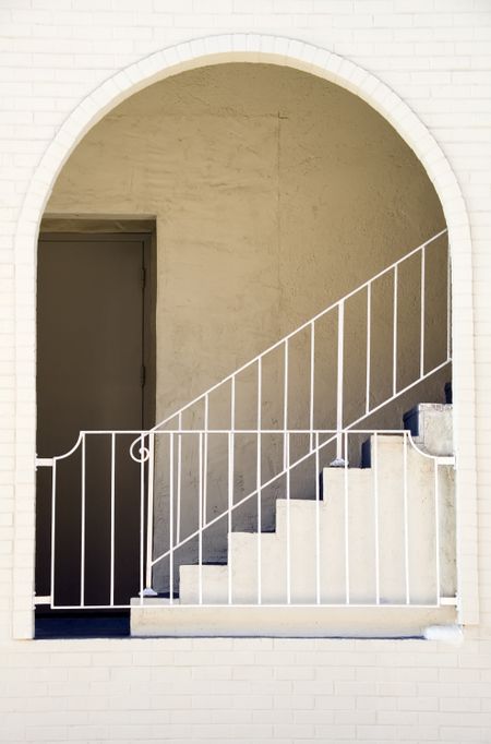 Arch and recessed door, guardrails, and stairway at side of white brick building in southwestern United States