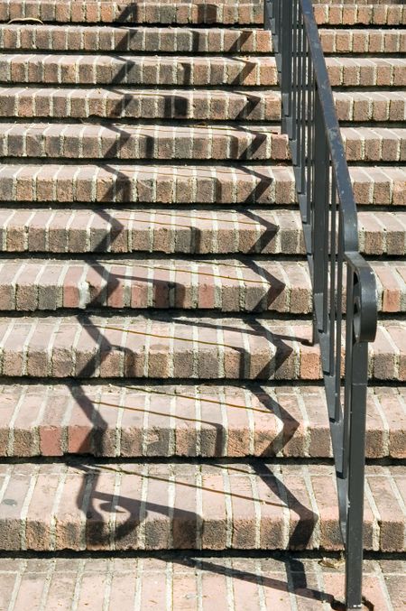 Zigzag shadows of black handrail on red brick stairway on college campus