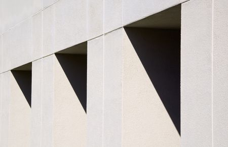 Three pennant-shaped shadowed recesses of exterior wall of university building in afternoon sunlight