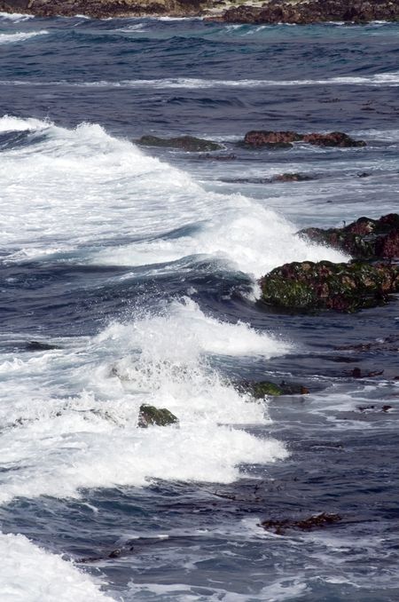 Ocean waves breaking white toward dark rocks near shore
