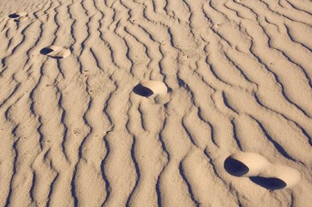 Four human footprints in rippled sand near sunset