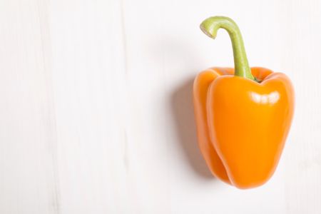 Fresh orange bell pepper on a light wooden kitchen surface