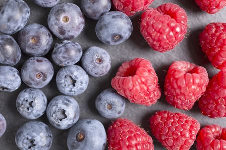 Fresh ripe summer raspberries and blueberries on black slate