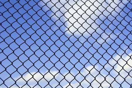 Barrier to dreams: Mesh fence with partly cloudy sky beyond