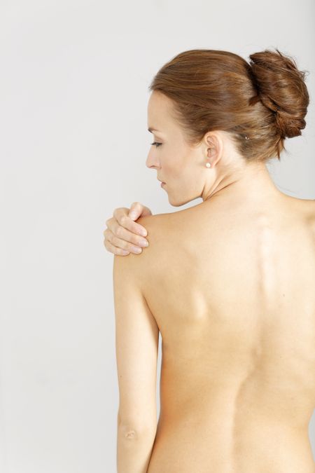 Young woman facing away massaging her shoulder from an ache or pain