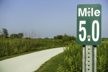 Marker at mile 5 by gravel path across prairie preserve for joggers, bicyclists, and hikers in west suburban Chicago, USA, in summer