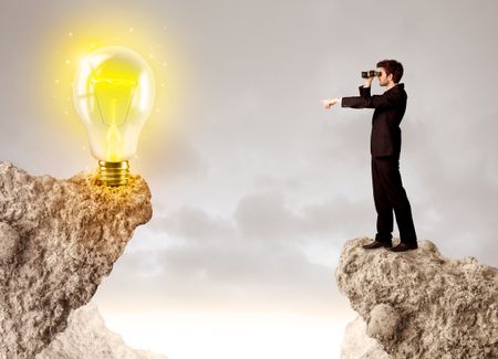 Businessman standing on the edge of mountain with an idea bulb on the other side 