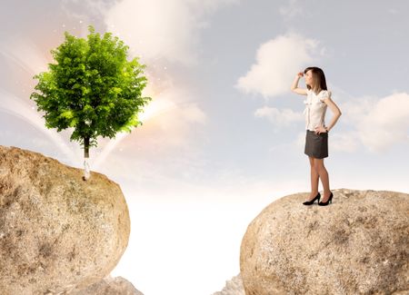 Businesswoman standing on the edge of rock mountain with a tree on the other side 