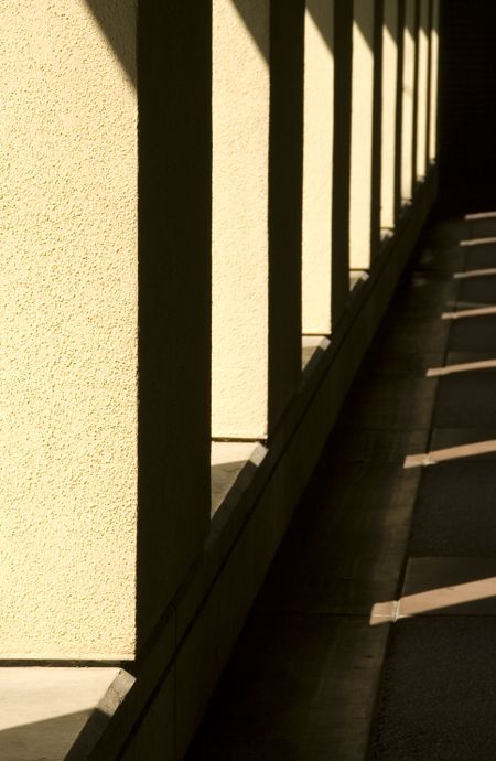 Passageway with sunlight and shadow outside building on college campus in southern California (focus on nearest stucco column)