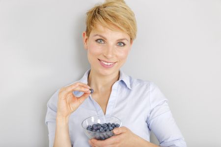 Beautiful young woman in a casual shirt enjoying fresh Blueberries at home