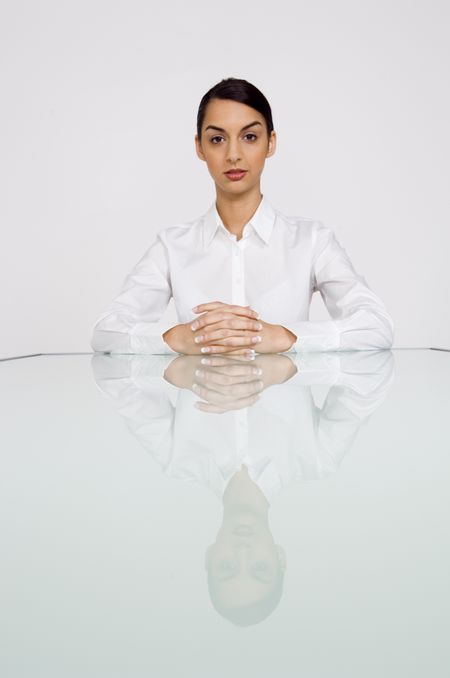 Businesswoman with fingers crossed at end of long reflective table.