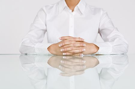 Close up of hands crossed on reflective table.