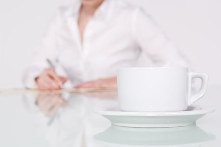 Close up of a coffee cup with businesswoman writing in background.