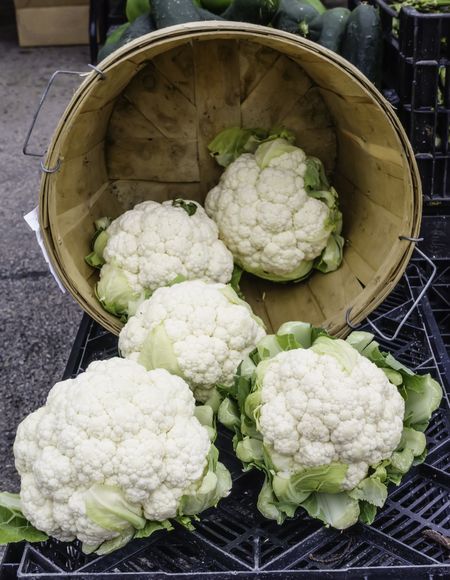 Five white cauliflowers, two still in the basket, on display cornucopia-style at a farmer's market (foreground focus)