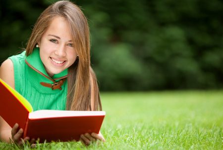 beautiful young female student reading a book outdoors