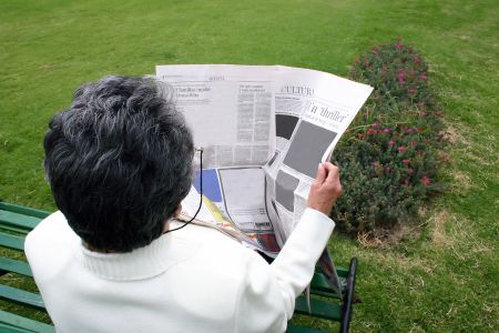 retired woman reading newspaper outdoors