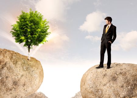 Businessman standing on the edge of rock mountain with a tree on the other side