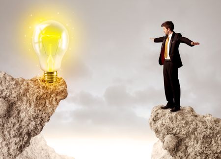 Businessman standing on the edge of mountain with an idea bulb on the other side