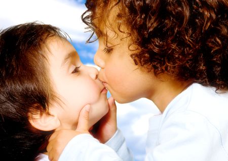 Cute baby brothers kissing over a blue sky in the background - soft focus