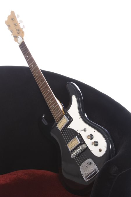 Electric guitar at an angle on red velour chair, white background