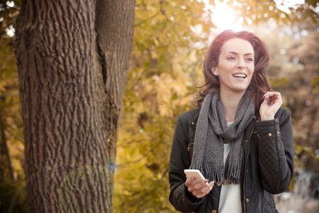 Young woman enjoying a autumn walk while texting with friends on her phone