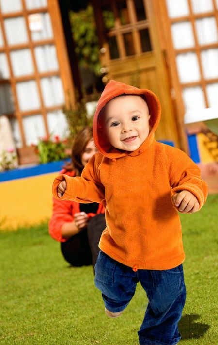 boy having fun outdoors while performing his first few steps on a sunny day at the garden - mum in the background