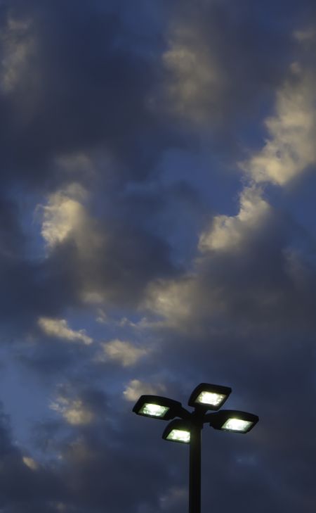 Top of outdoor lightpole with four electric lights against evening sky