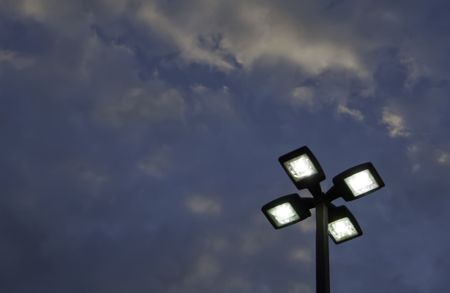 Top of outdoor lightpole with four electric lights against evening sky