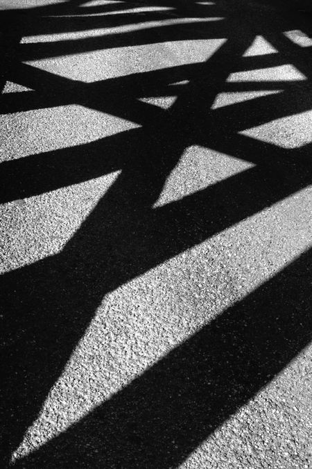 Abstract of structural shadows: Crisscross of long shadows on public park land beneath a timber approach span of a railroad bridge built in 1898 across the Illinois River, in black and white