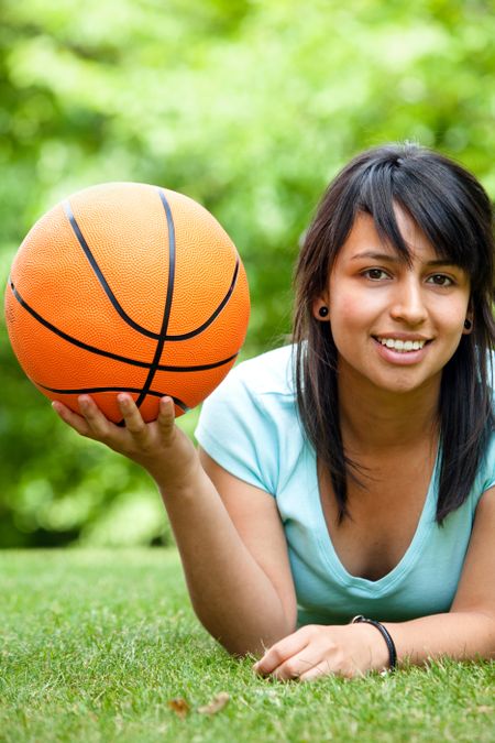 Girl holding a basketball lying on the grass outdoors