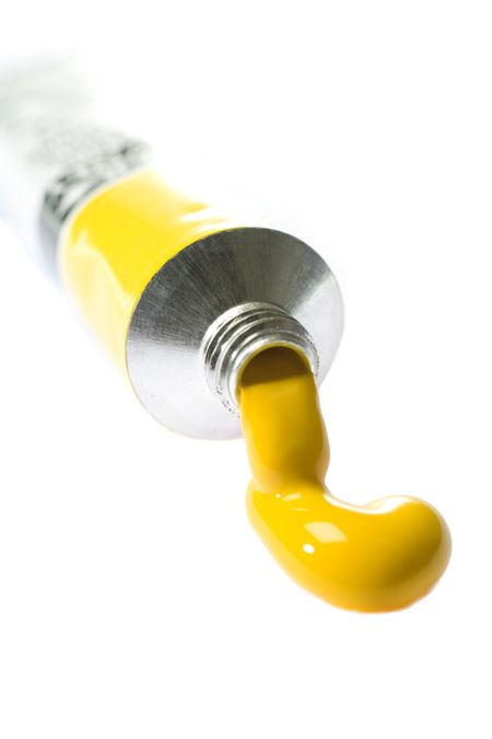 Yellow paint coming from tube on white background
