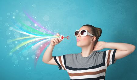 Beautiful girl blowing abstract colorful bubbles and lines on blue background