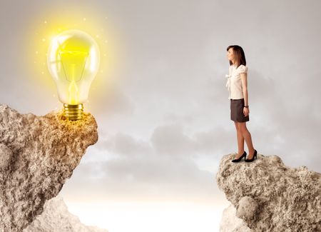 Businesswoman standing on the edge of rock mountain with an idea bulb on the other side 