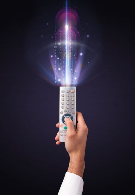Hand holding a remote control, shining numbers and letters coming out of it 