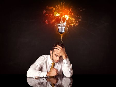 Depressed businessman sitting under a blowing idea bulb