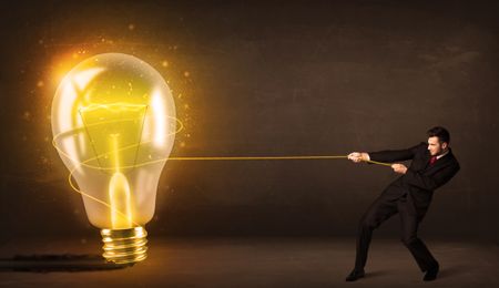 Business man pulling a big bright glowing light bulb concept on background