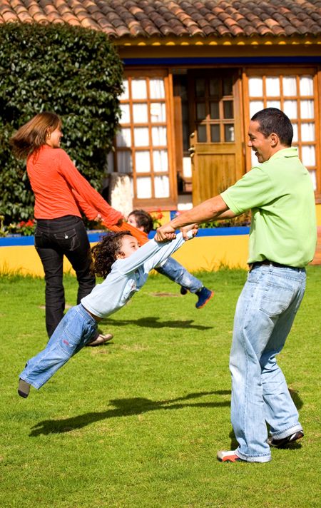 happy family having fun outdoors at home - parents making kids go round in the air